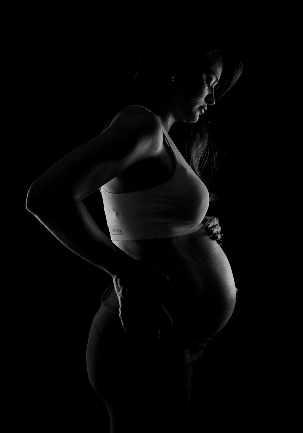 grayscale photo of pregnant woman near black surface