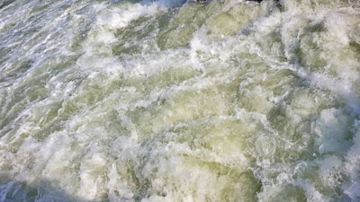 Foamy and turbulent water surface with churning waves and a mixture of white and green hues.