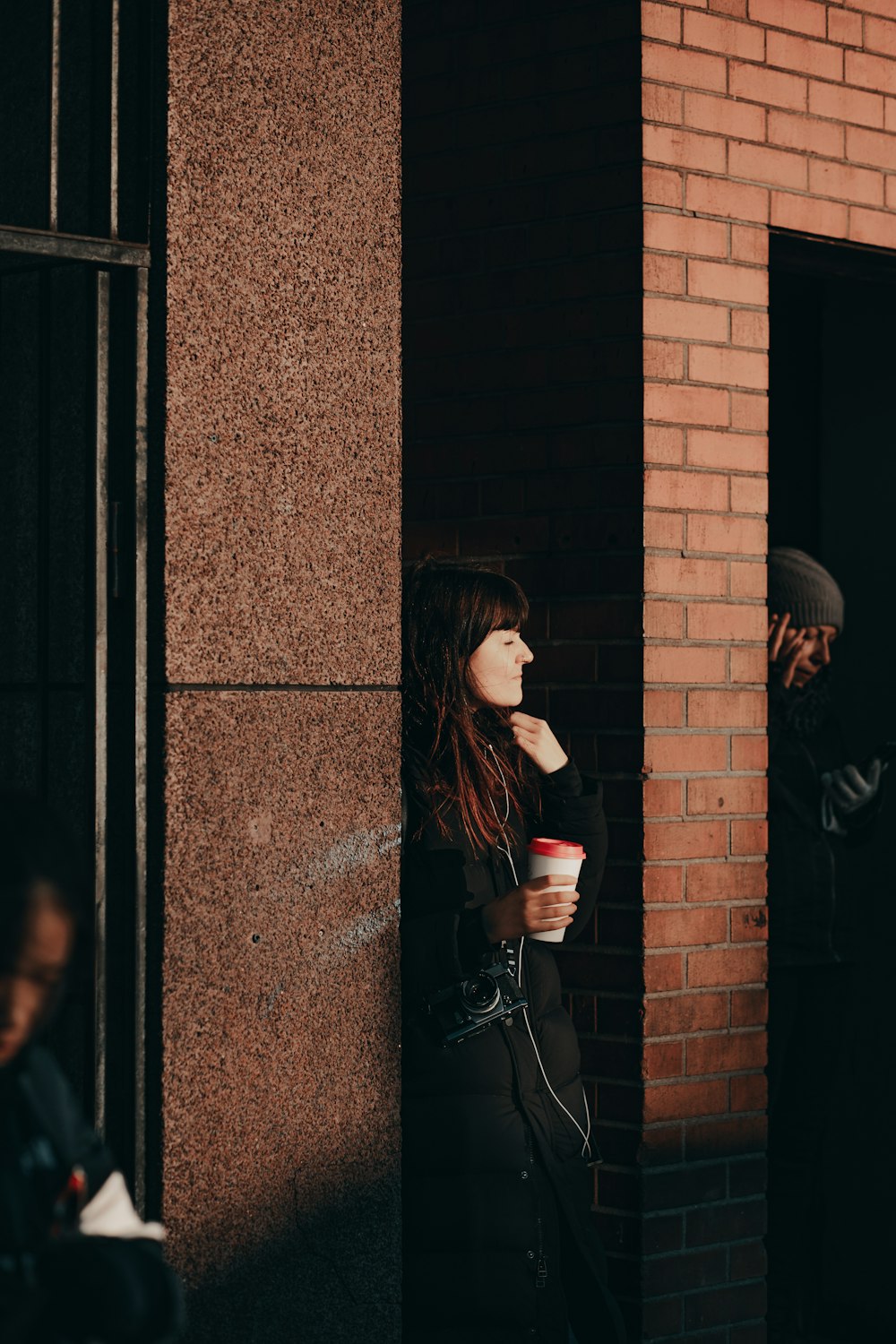 a woman standing next to a brick building holding a cup of coffee