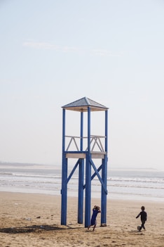 two person walking beside tower on beach