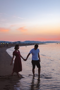 man and woman walking on seashore and holding hands during golden hour