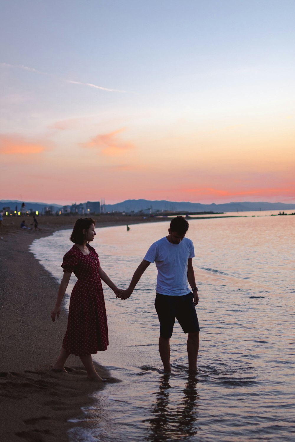 man and woman walking on seashore and holding hands during golden hour
