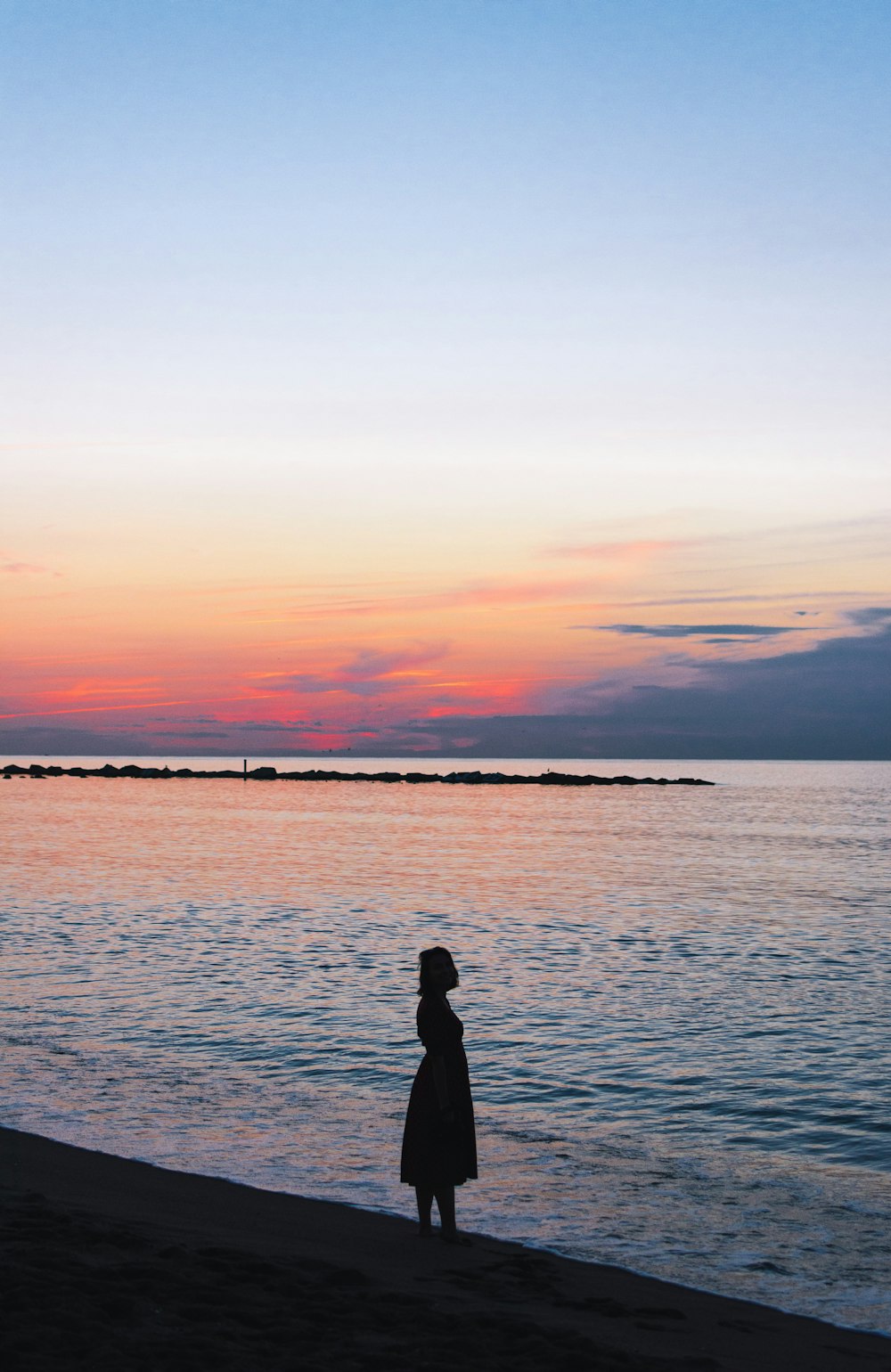 Frau steht während der goldenen Stunde am Meeresufer