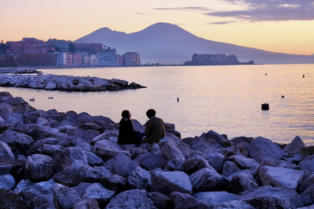 man in black jacket sitting on rock near body of water during daytime