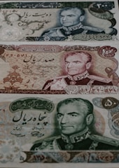 Three different Iranian banknotes featuring detailed engravings of a man's portrait dressed in military attire. The notes are adorned with intricate floral and scrollwork patterns, accompanied by Persian script.