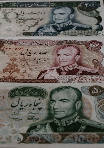 Three different Iranian banknotes featuring detailed engravings of a man's portrait dressed in military attire. The notes are adorned with intricate floral and scrollwork patterns, accompanied by Persian script.