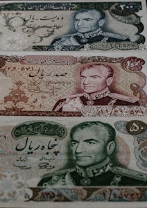 Three different Iranian banknotes featuring detailed engravings of a man's portrait dressed in military attire. The notes are adorned with intricate floral and scrollwork patterns, accompanied by Persian script.