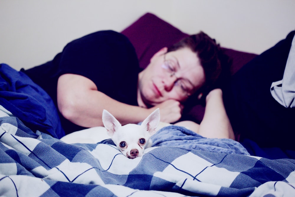man lying down in bed beside white dog