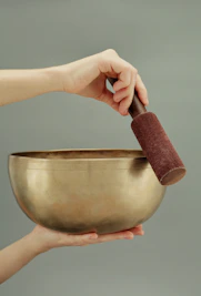 Close-up of hands gently holding a Tibetan singing bowl with a soft green background.