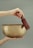 A hand holds a large, golden singing bowl, with another hand gently holding a mallet over the bowl's rim. The background is a soft, muted green, creating a calm atmosphere.