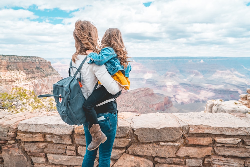 woman in blue denim jacket and blue denim jeans carrying blue backpack standing on brown rock