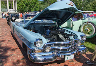 A beautifully restored antique car displayed at a sunny outdoor car show.