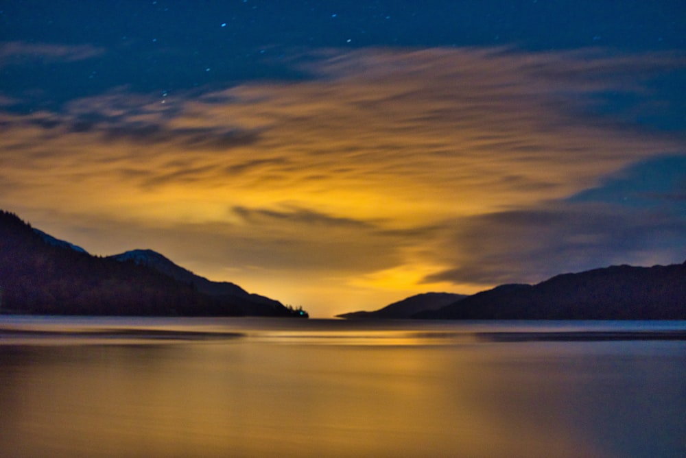 silhouette of mountain near body of water during sunset