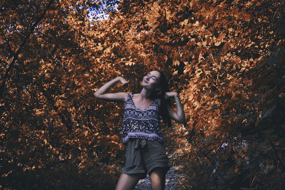 woman in black and white floral sleeveless dress standing near brown leaves tree during daytime