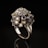A luxurious and ornate ring featuring numerous small, multifaceted gemstones in various colors is elegantly showcased. The ring is crafted from shiny metal and is set against a stark black background, highlighting its intricate design and vibrant gemstones.