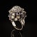 A luxurious and ornate ring featuring numerous small, multifaceted gemstones in various colors is elegantly showcased. The ring is crafted from shiny metal and is set against a stark black background, highlighting its intricate design and vibrant gemstones.