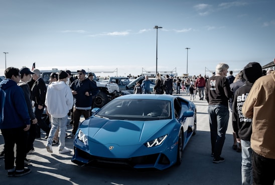 A group of car enthusiasts gathered around a variety of sleek, customized cars on a sunny Saturday.