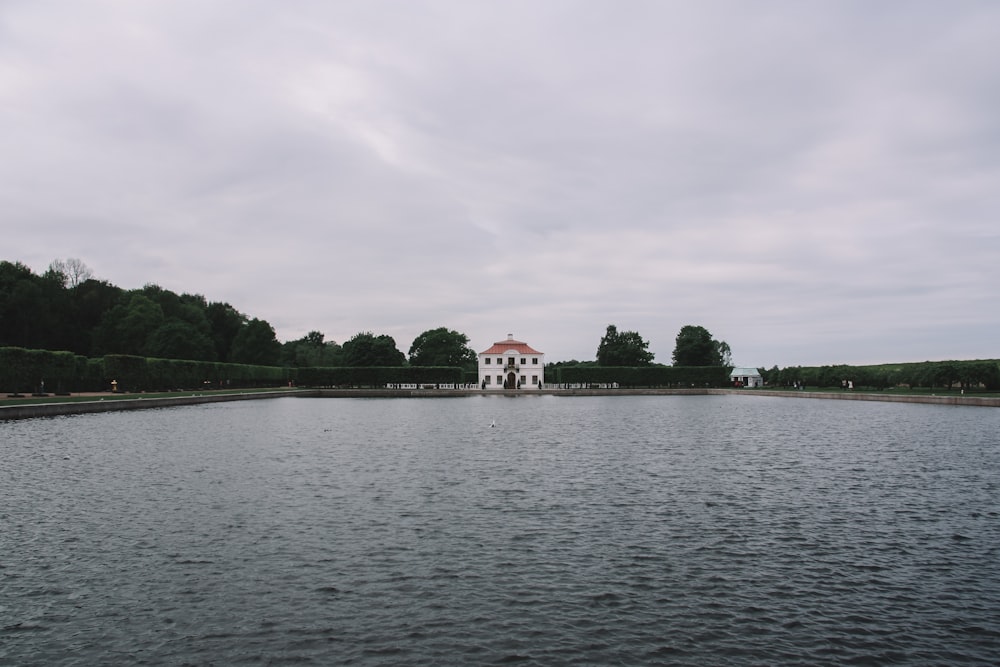 white and red house near green trees and body of water during daytime