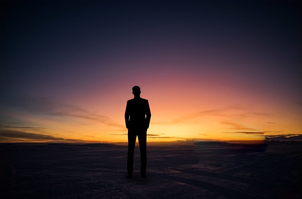 silhouette of man standing on beach during sunset