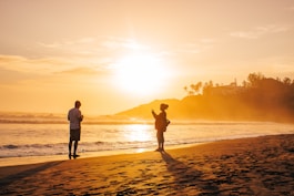 silhouette of man and woman holding hands on beach during sunset