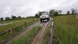 A 4x4 vehicle crossing a shallow lagoon stream under a bright blue sky.