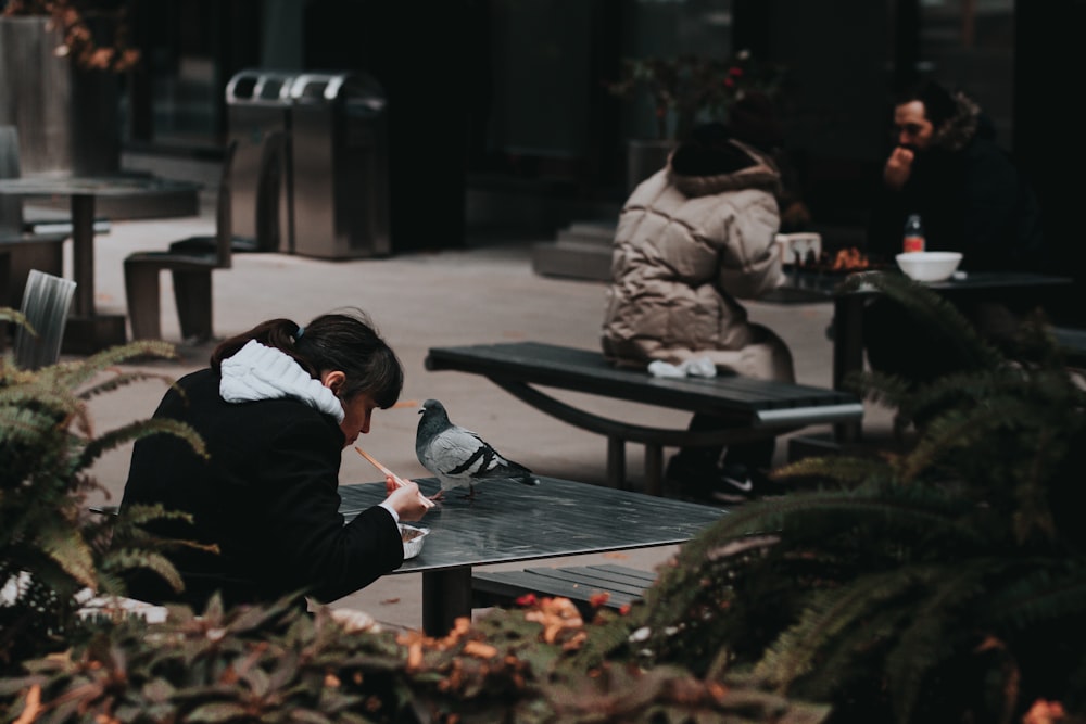 a woman sitting at a table with a bird on her lap