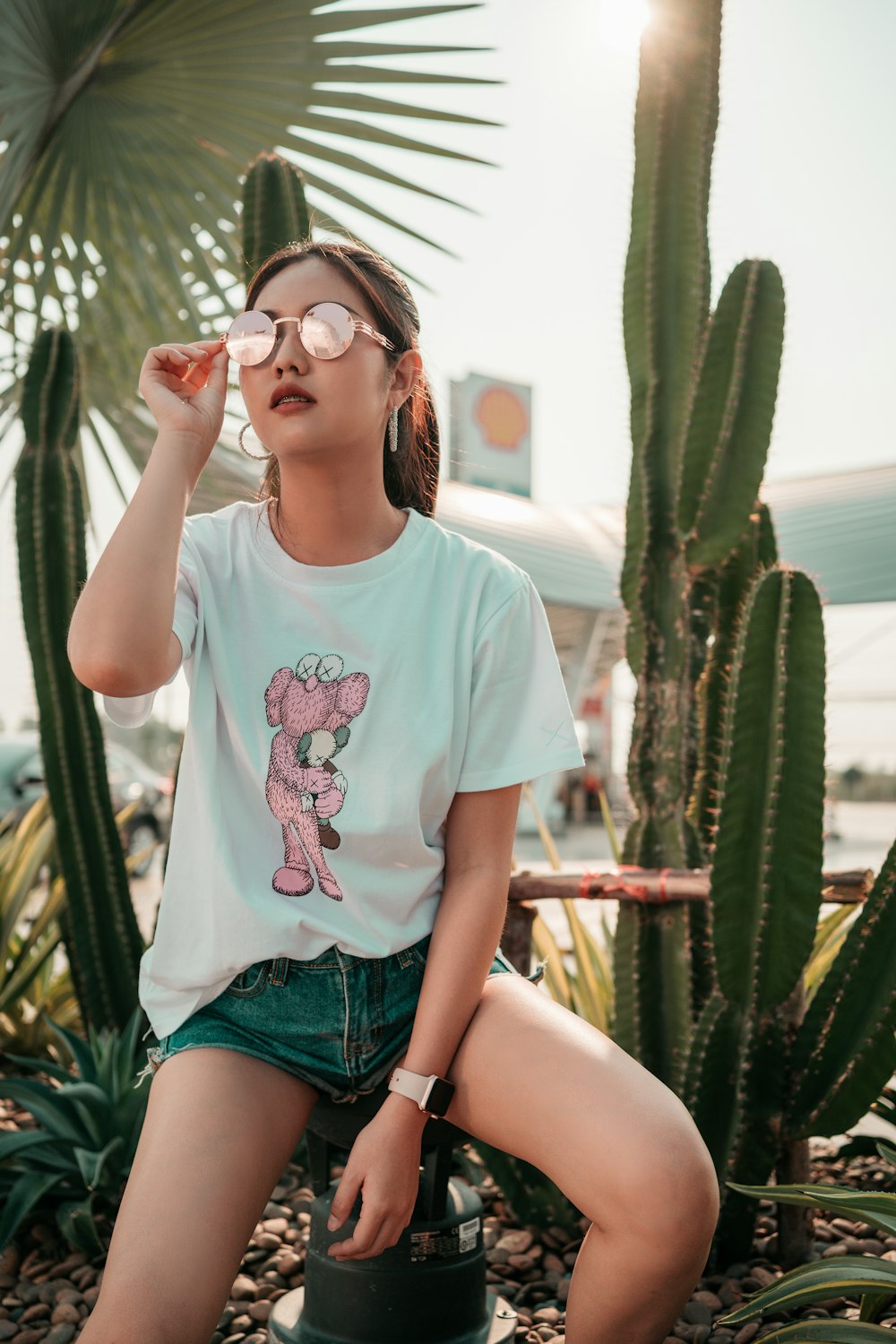 Femme en t-shirt à col rond blanc et short en jean bleu assise sur un banc en bois marron