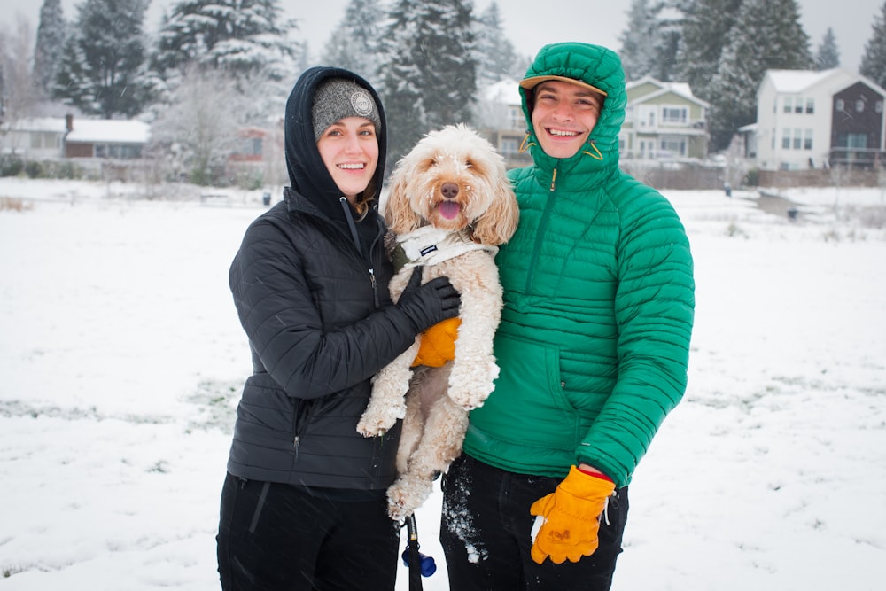 a man and a woman holding a dog in the snow