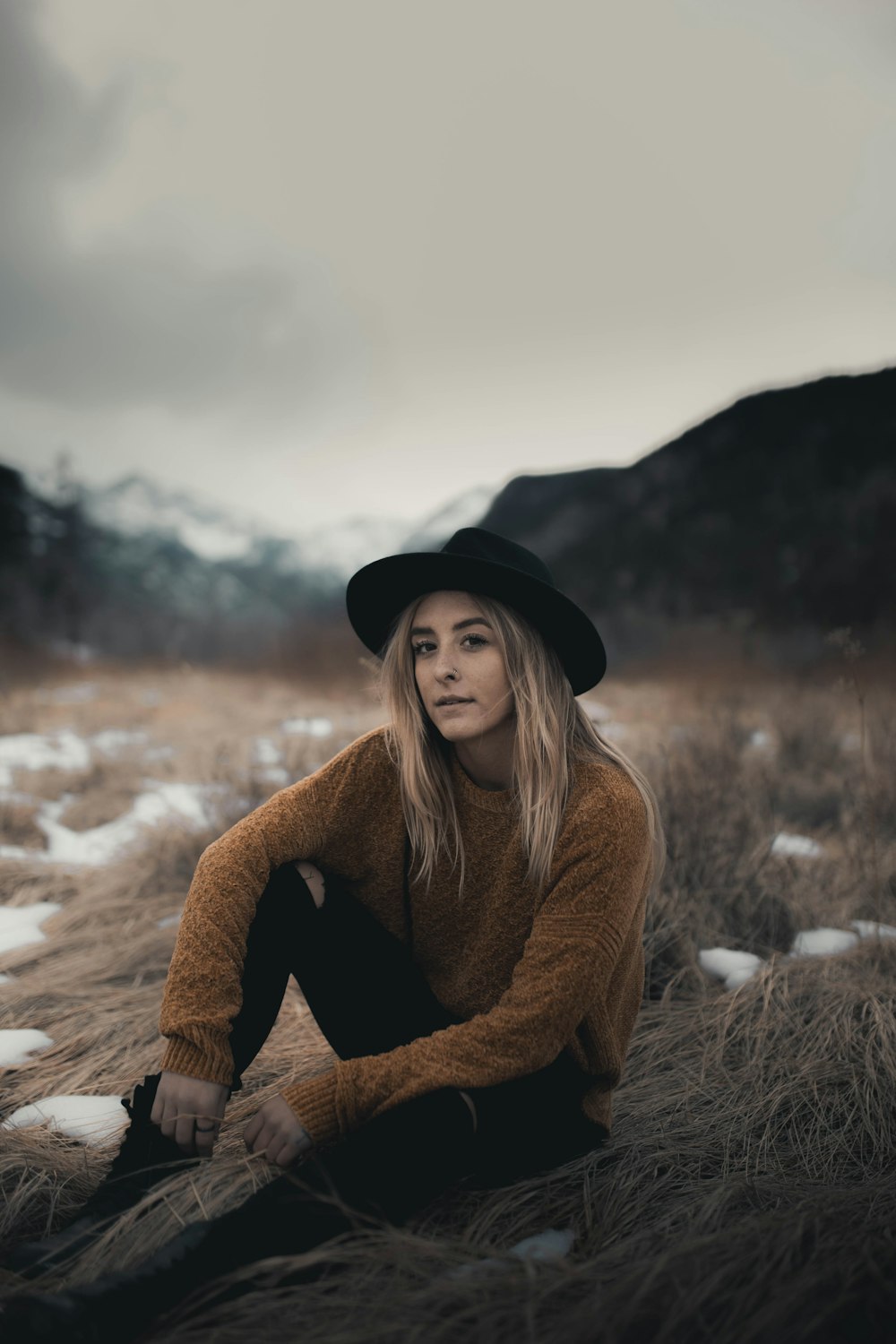 woman in brown sweater and black hat sitting on snow covered ground during daytime