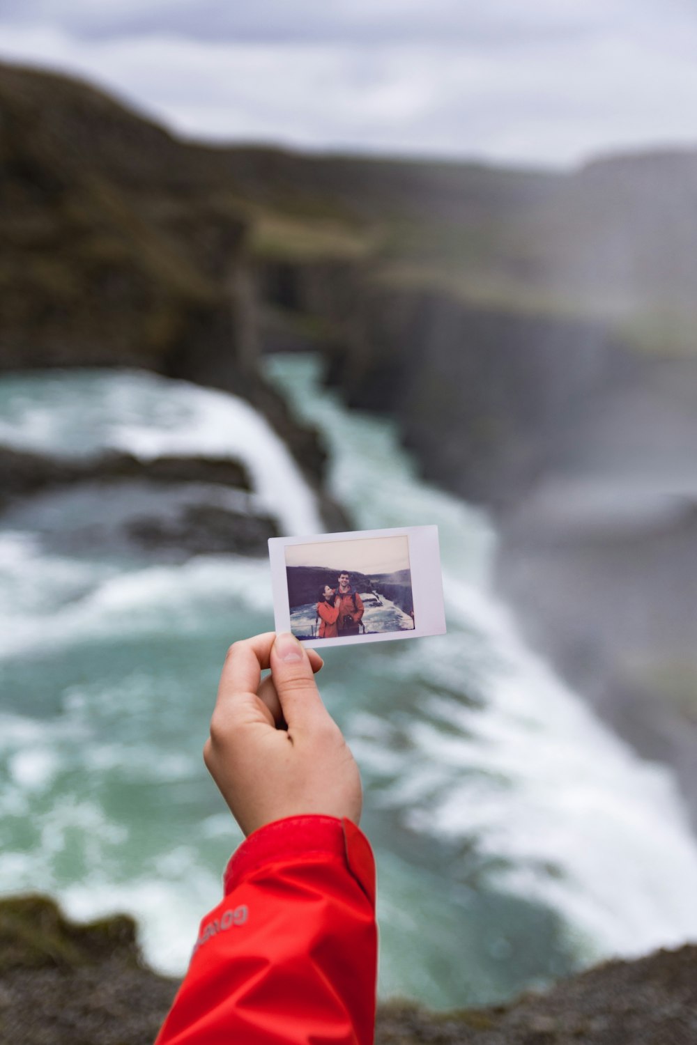 Eine Person, die ein Polaroid mit einem Wasserfall im Hintergrund hochhält