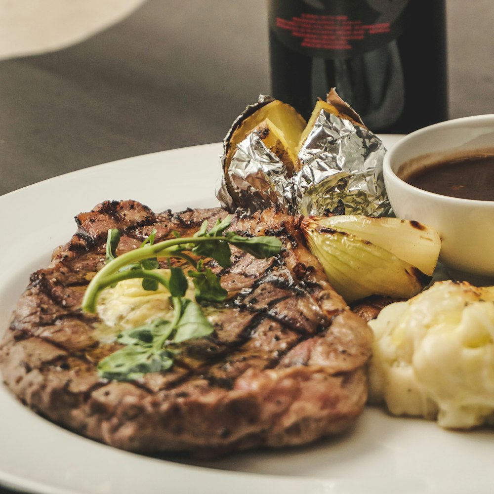 a white plate topped with meat and potatoes next to a bottle of wine