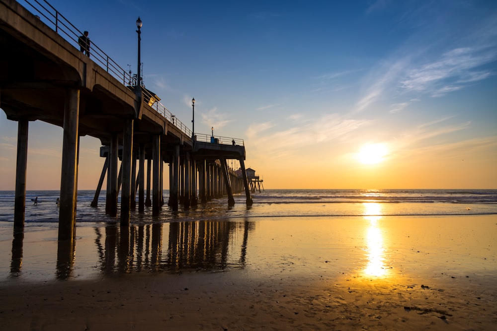 a pier on a beach with the sun setting in the background