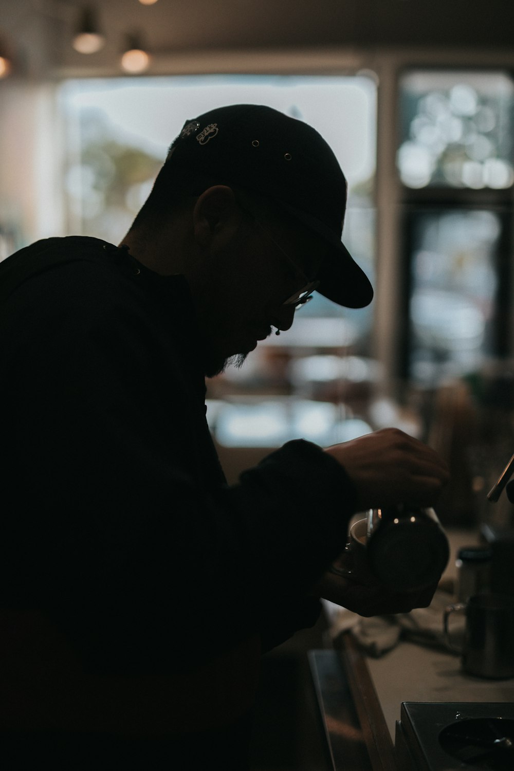 a man in a black shirt and cap is pouring a cup of coffee