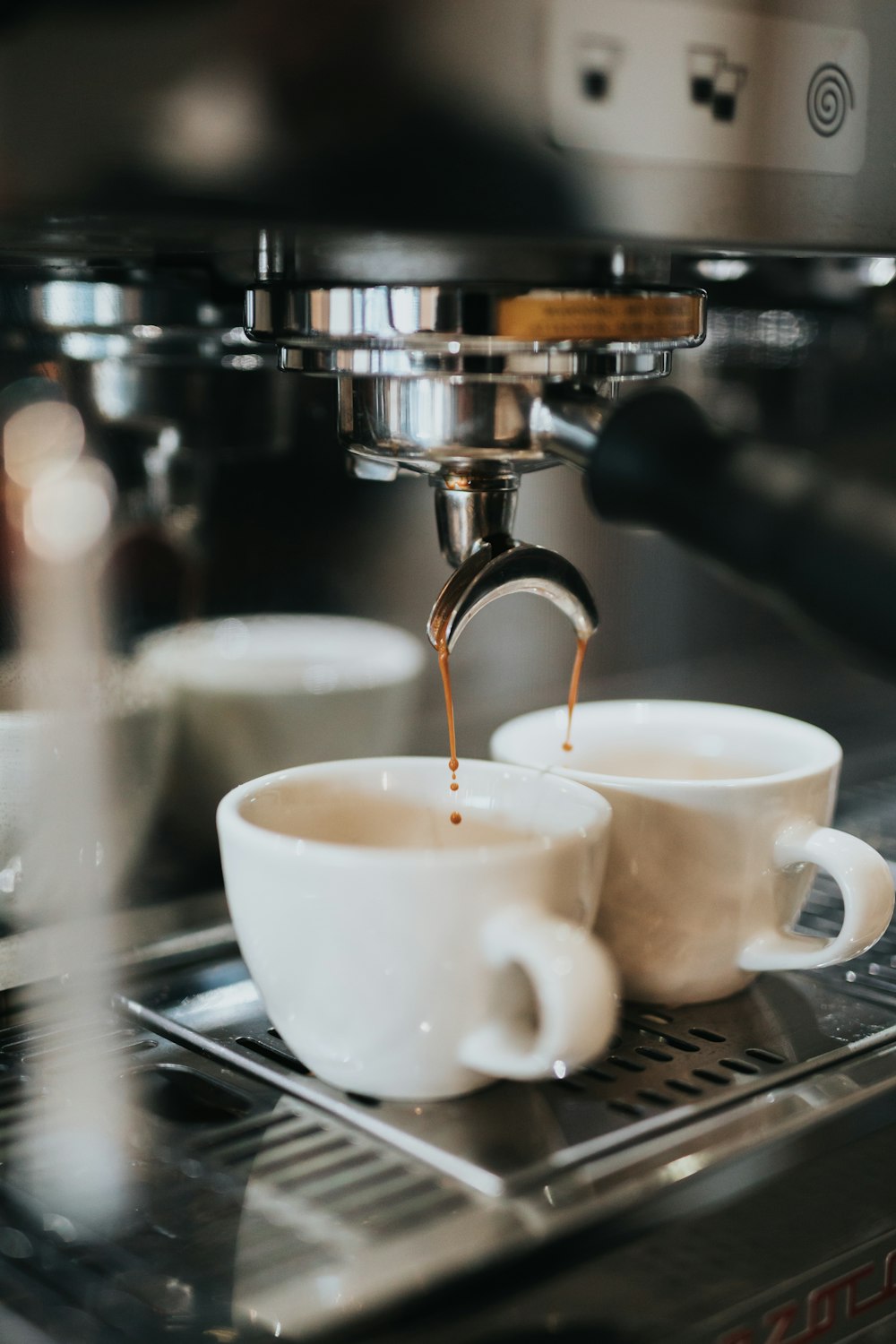 two cups of coffee being poured into a coffee machine