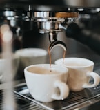 two cups of coffee being poured into a coffee machine