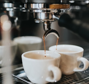 two cups of coffee being poured into a coffee machine