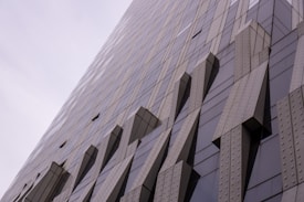A tall building with a modern architectural design, featuring an exterior of glass panels and unique, protruding geometric structures that create an abstract pattern across the façade.