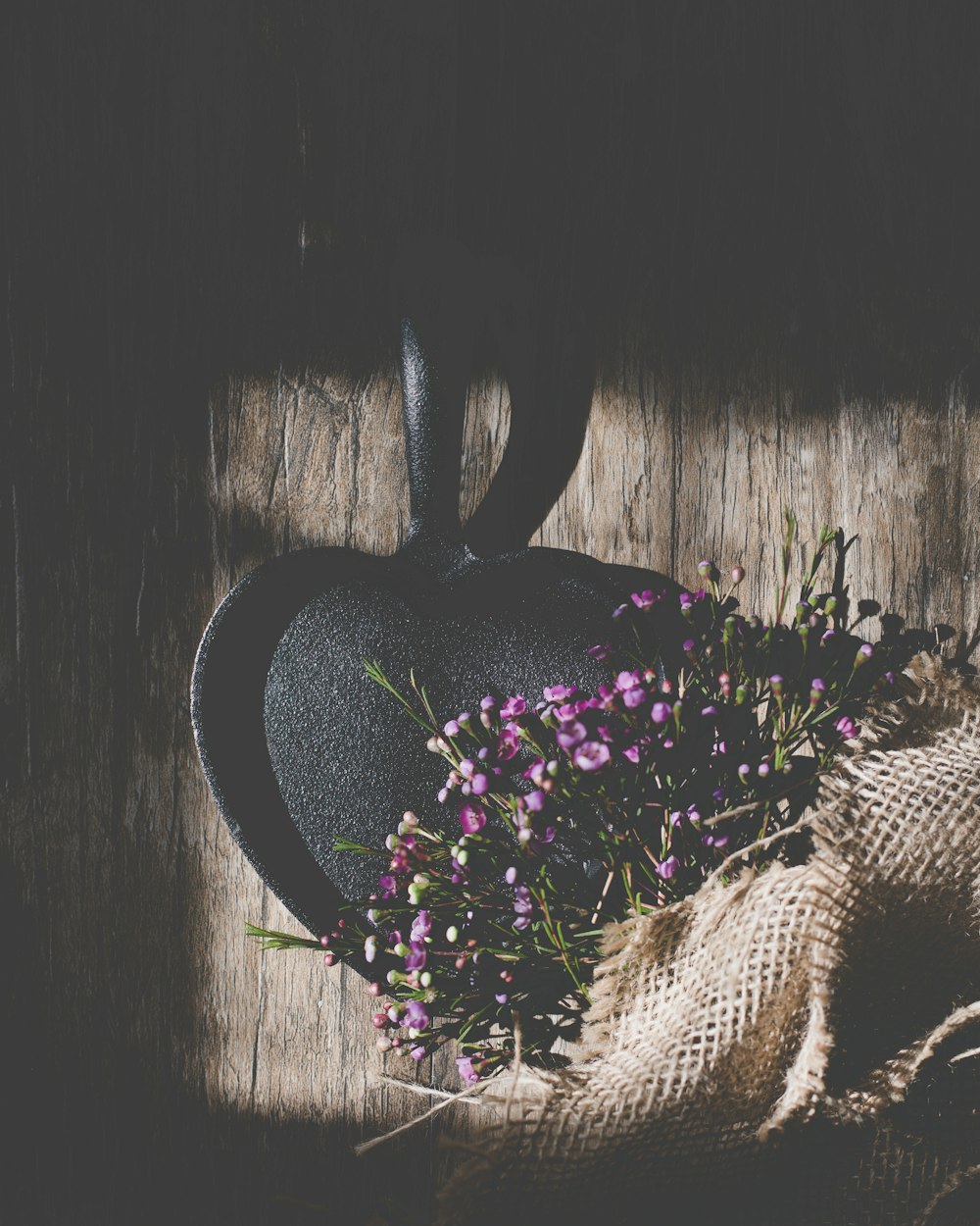 eine schwarze herzförmige Vase mit lila Blumen darin