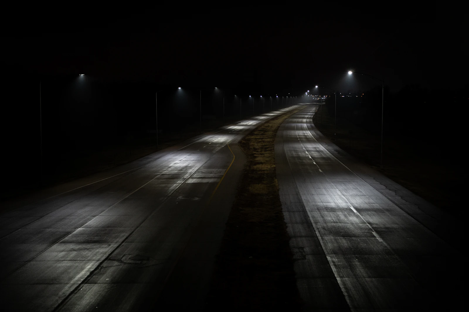 An empty road at night lit by a line of overhead lamps