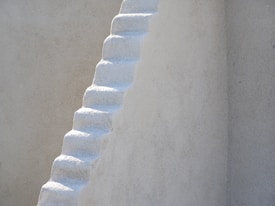 A set of white, uneven, narrow steps ascends diagonally against a plain, light-colored wall.