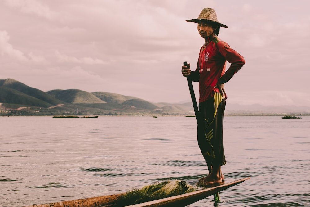 man in red dress shirt and brown pants wearing brown hat standing on brown wooden log