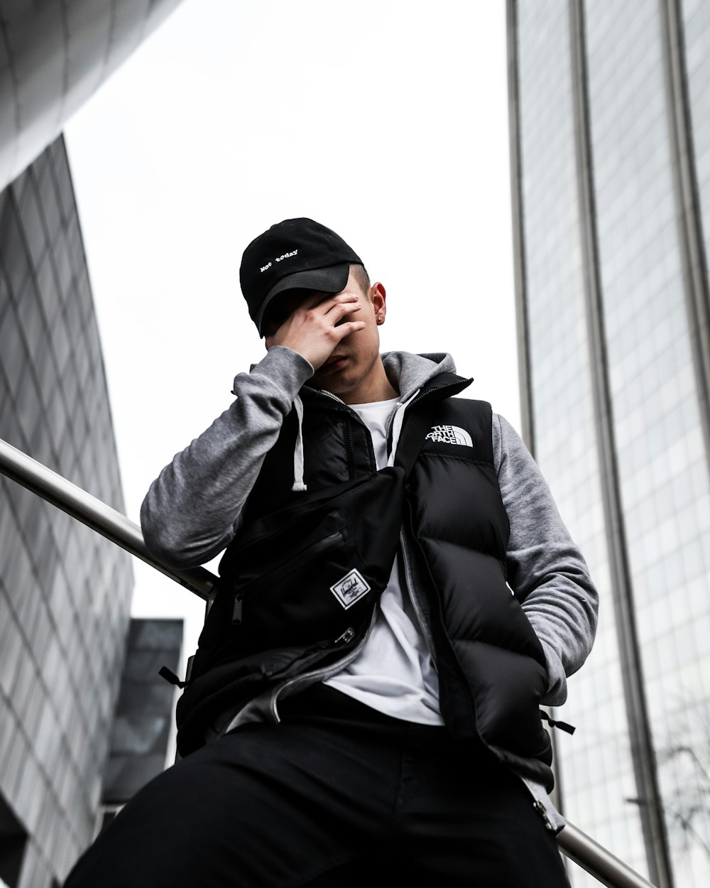 man in black jacket and black cap sitting on gray metal railings during daytime