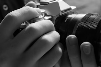 grayscale photo of person holding black and silver nikon dslr camera