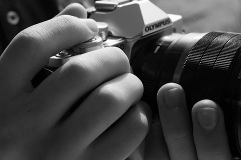 grayscale photo of person holding black and silver nikon dslr camera