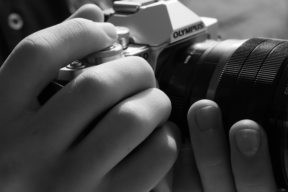 grayscale photo of person holding black and silver nikon dslr camera