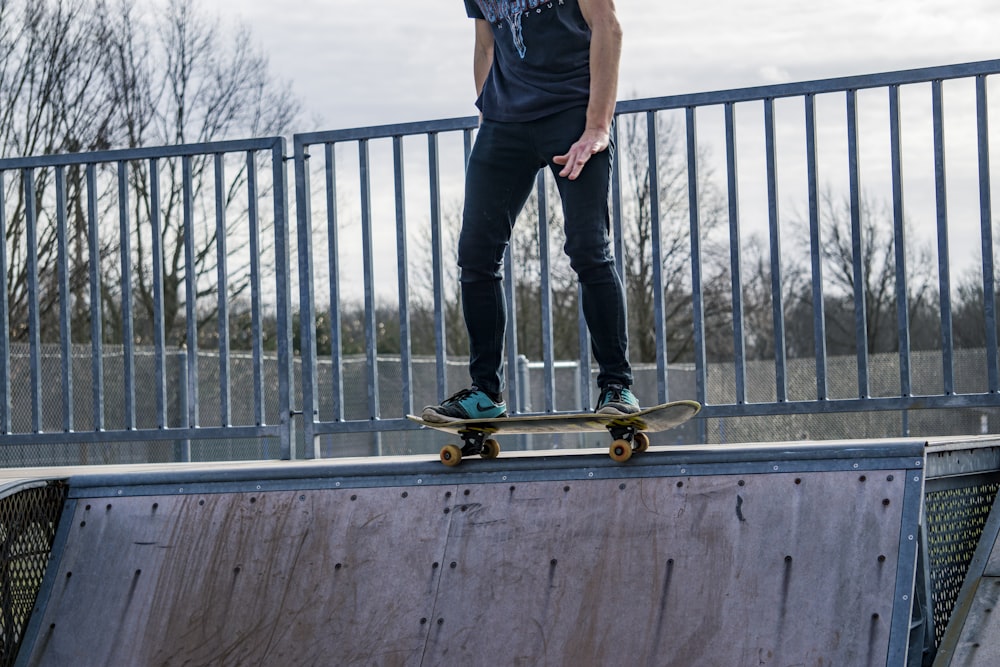 man in black t-shirt and blue denim jeans standing on wooden dock during daytime