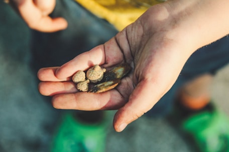 Close-up of hands holding mineral samples with mining equipment blurred behind.
