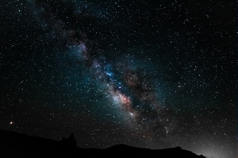 silhouette of mountain under blue sky with stars during night time