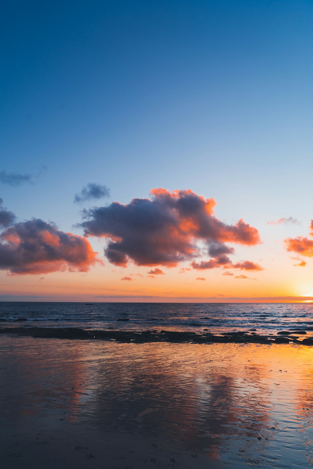 the sun is setting over the ocean with clouds in the sky