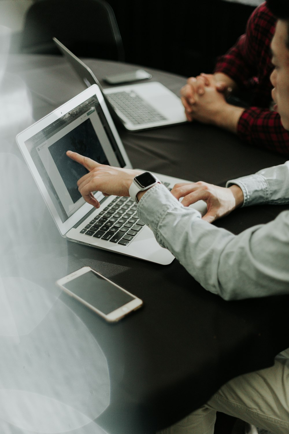 Dos personas sentadas en una mesa con computadoras portátiles